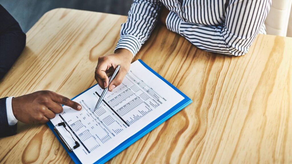 2 personen waarvan 1 wijst naar een papier met cijfers en de ander een pen in de hand heeft