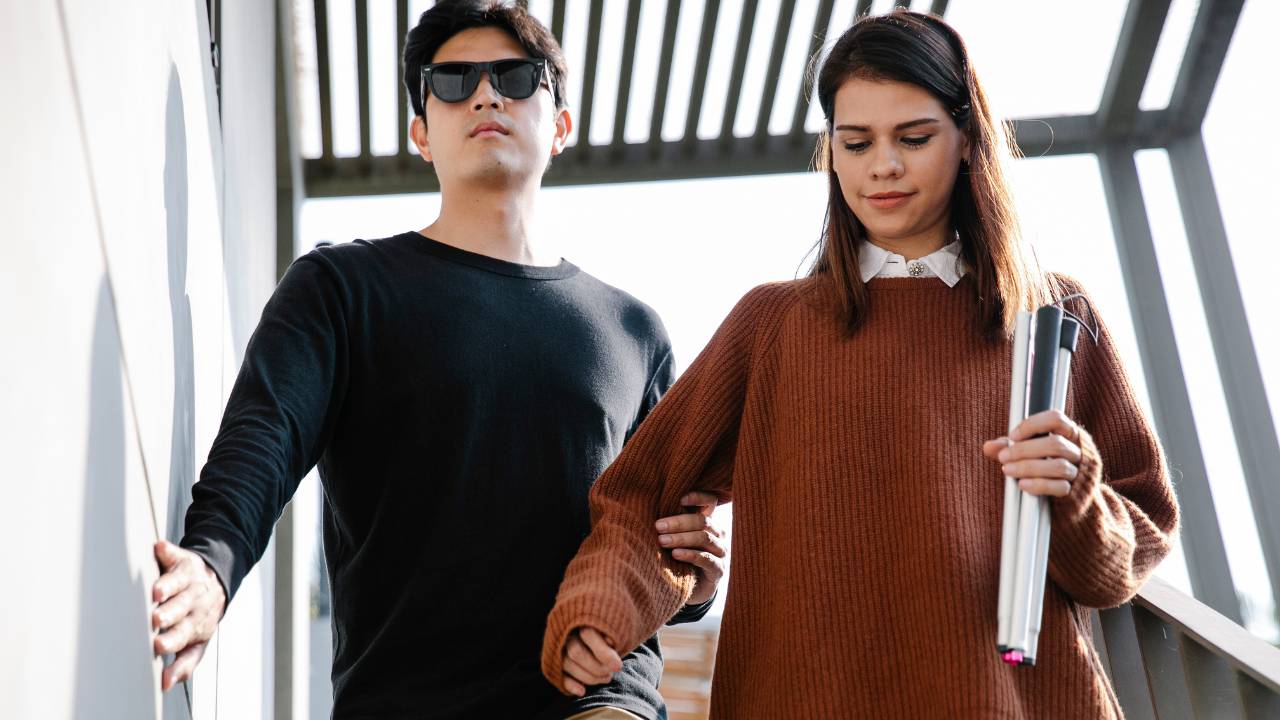 blinde man die van de trap begeleid wordt door vrouw